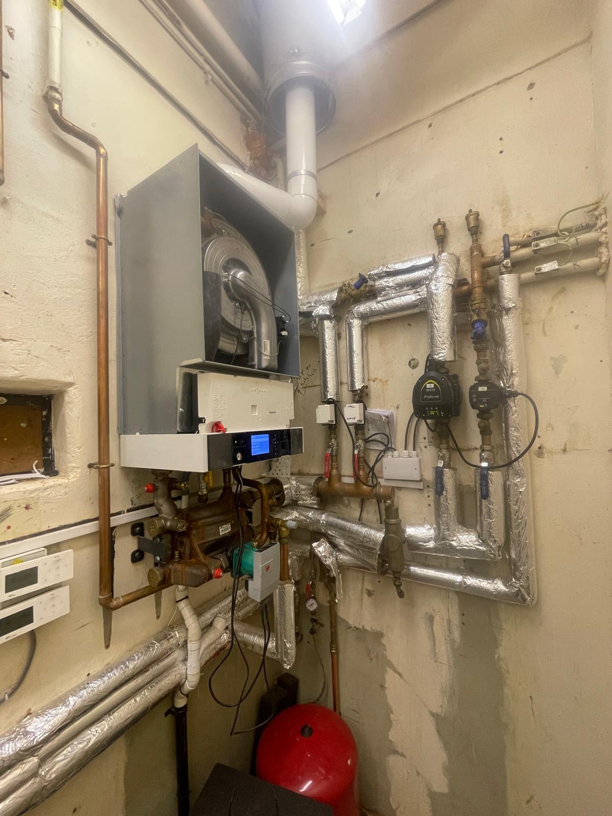 Commercial plant room with wall-mounted boiler, insulated pipework and circulation pumps